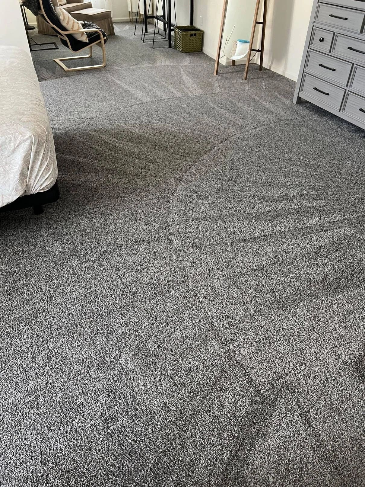 Bedroom with patterned gray carpet, a bed, chair, table, mirror, and dresser.